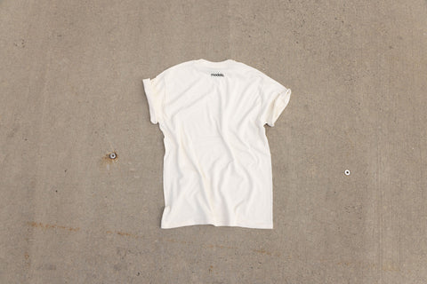 A white short-sleeve t-shirt laid flat on a textured gray concrete surface, viewed from a top-down perspective. "models." logo printed below the neckline.