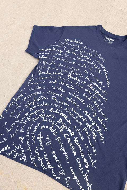 A navy blue t-shirt with a white fingerprint script graphic, laid flat on a light beige textured surface. The brand name 'model.'