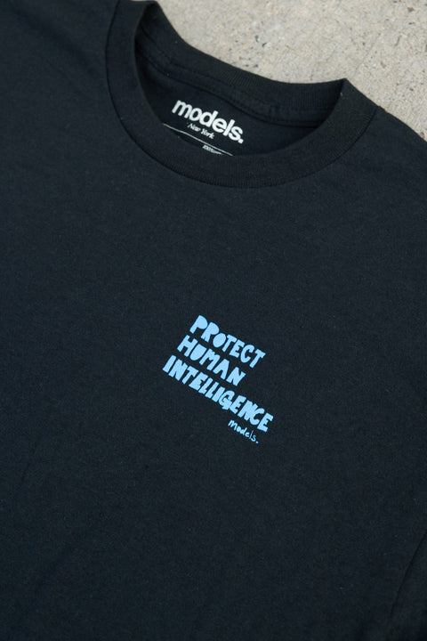 Close-up of a black crewneck t-shirt with a light blue graphic text reading 'PROTECT HUMAN INTELLIGENCE' on the chest. The inside collar shows the brand 'models.'