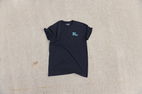 A black short-sleeve t-shirt with a small light blue "Protect Human Intelligence" graphic on the left chest, laid flat on a textured concrete surface.