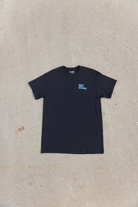 A black short-sleeve crewneck t-shirt with a small light blue graphic on the left chest, laid flat on a textured concrete surface.