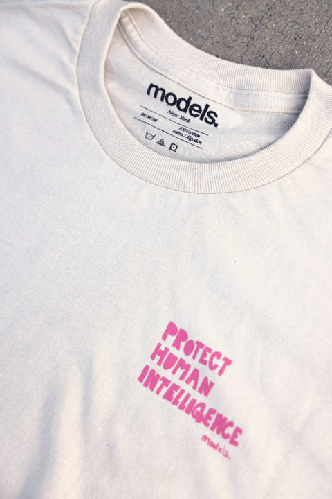 Close-up of a white crewneck t-shirt with pink text reading 'PROTECT HUMAN INTELLIGENCE' on the chest. The inside collar shows the 'models.'