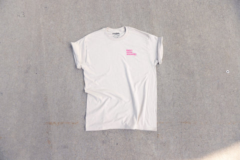 A white short-sleeve crewneck t-shirt with a small pink "Protect Human Intelligence" graphic on the left chest, laid flat on a textured gray concrete surface.