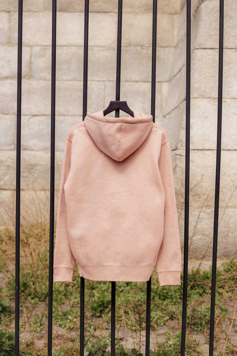 Dusty pink hoodie hanging on a black metal fence with a stone wall background
